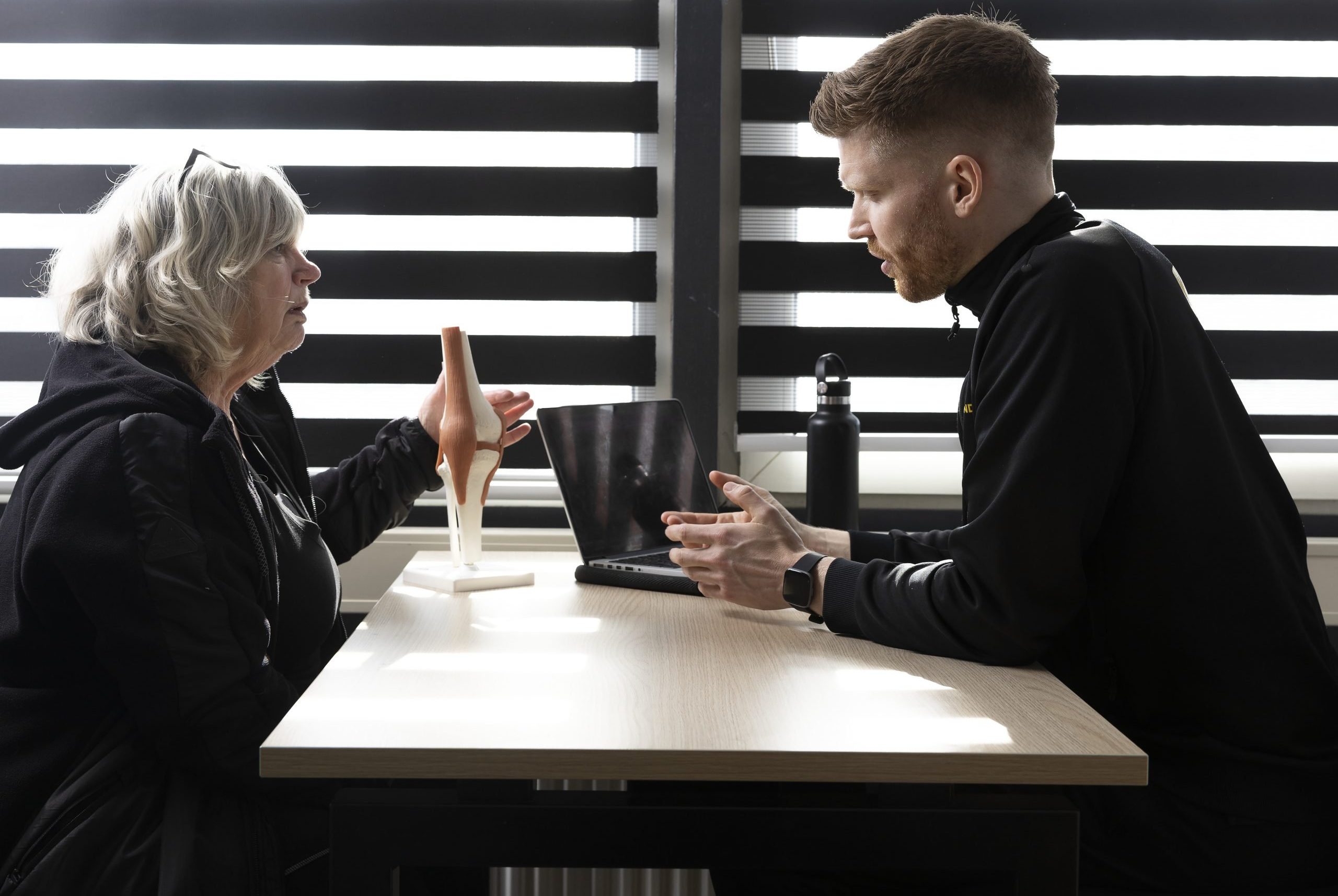 Trainer legt kniemodel uit aan cliënt tijdens intake gesprek aan tafel