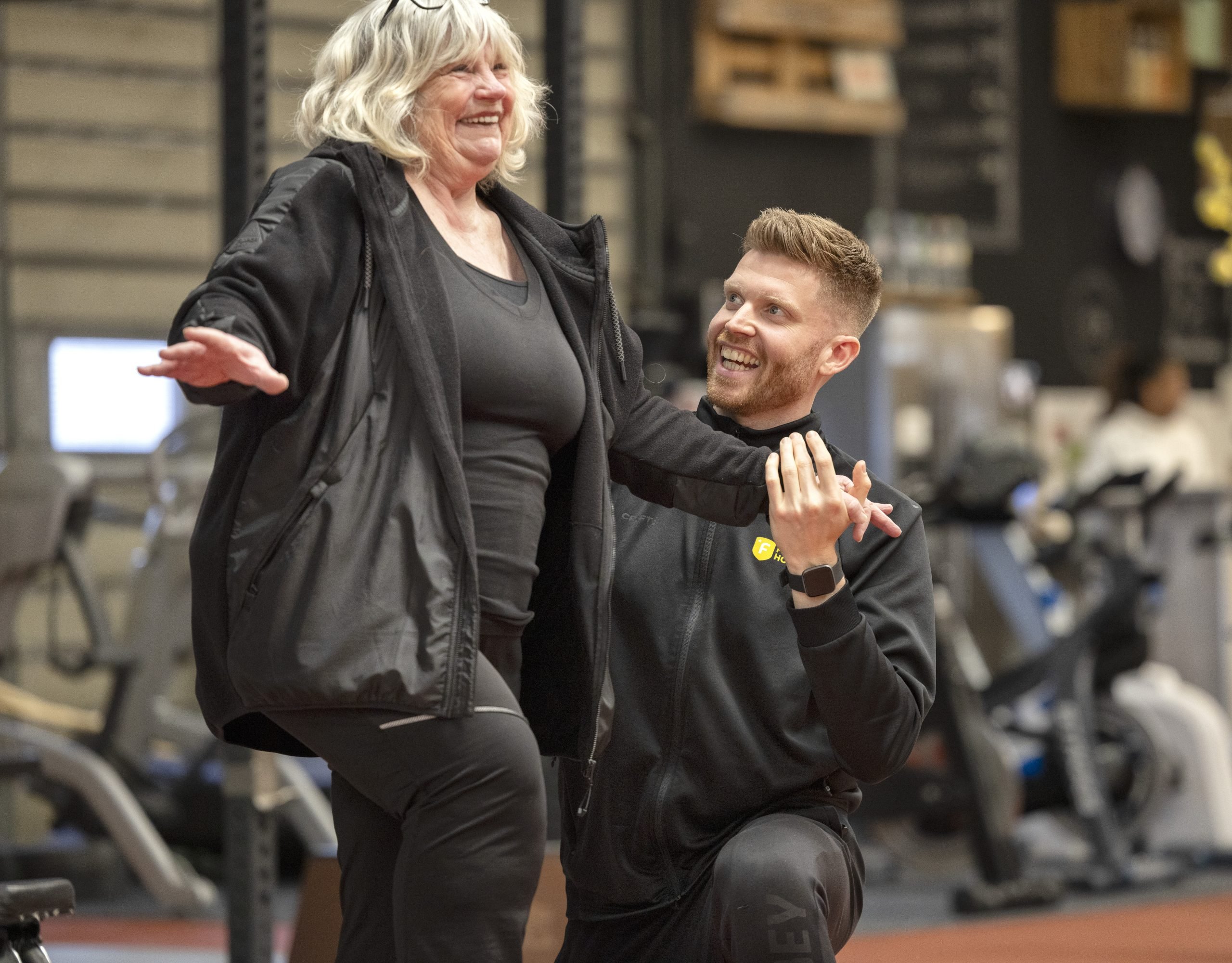 Oudere vrouw lacht met personal trainer tijdens coaching moment in de sportschool