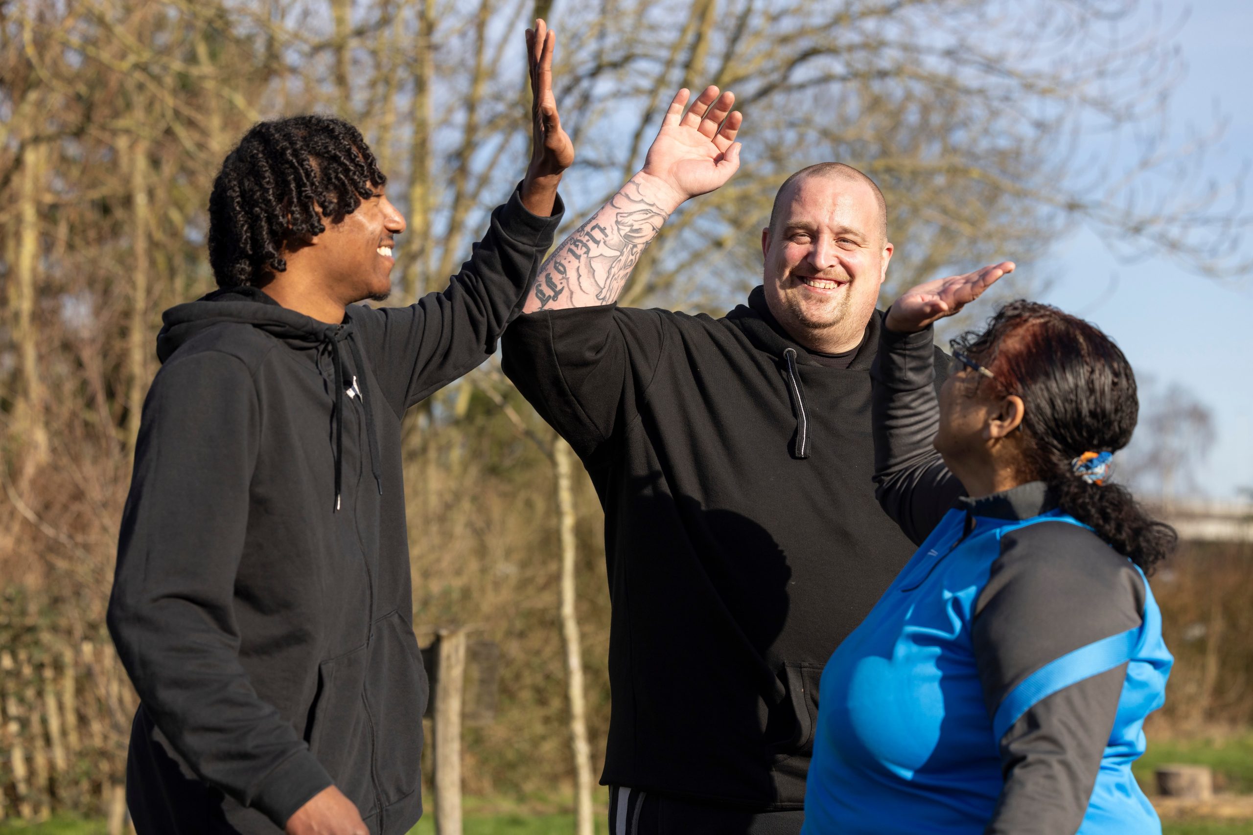 Drie deelnemers geven elkaar high five lachend buiten na training