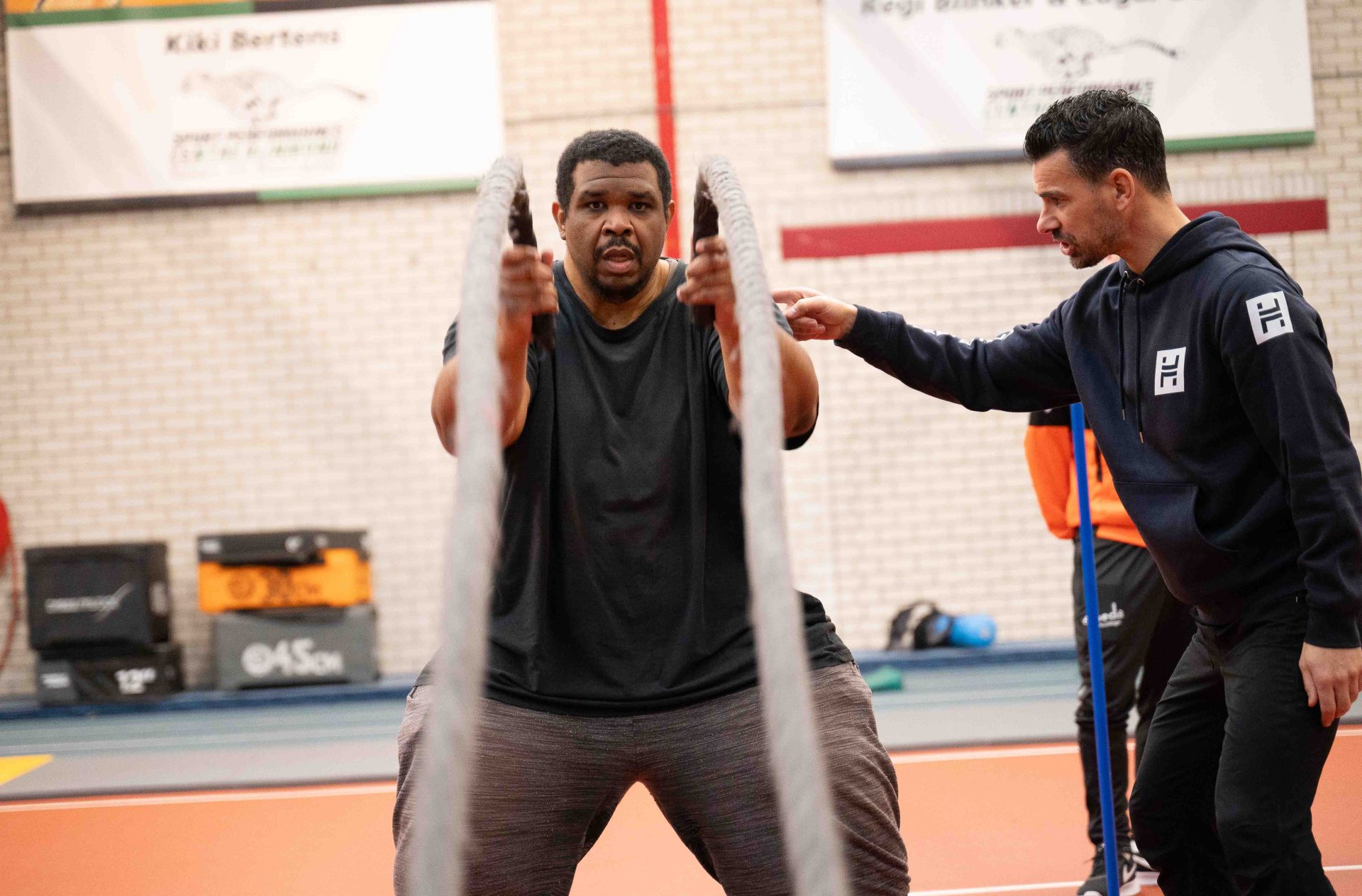 Man doet battle rope oefening onder begeleiding van coach in de sportschool