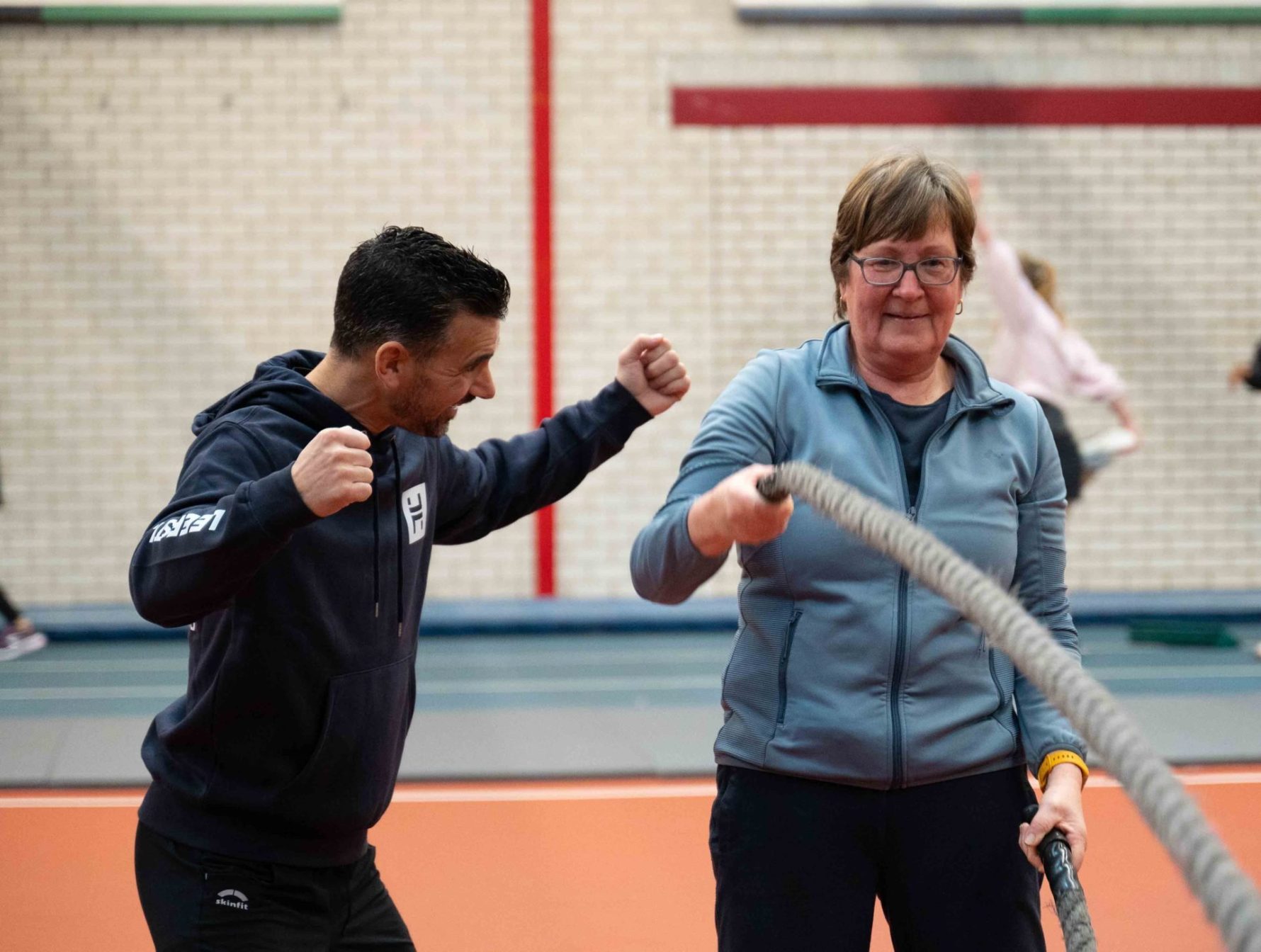 Coach moedigt vrouw enthousiast aan tijdens battle rope oefening