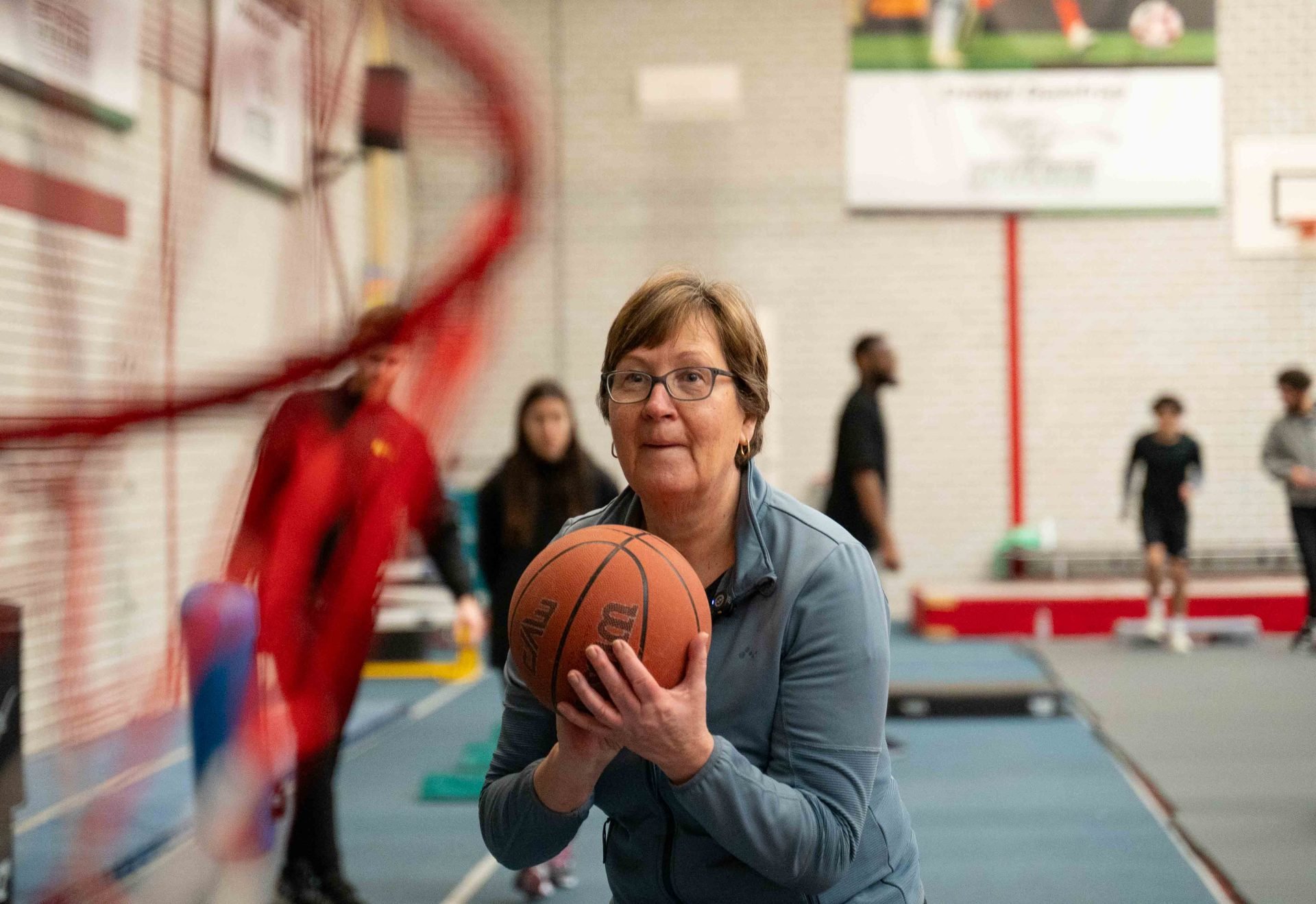 Oudere vrouw houdt basketbal vast klaar om te schieten in de sporthal