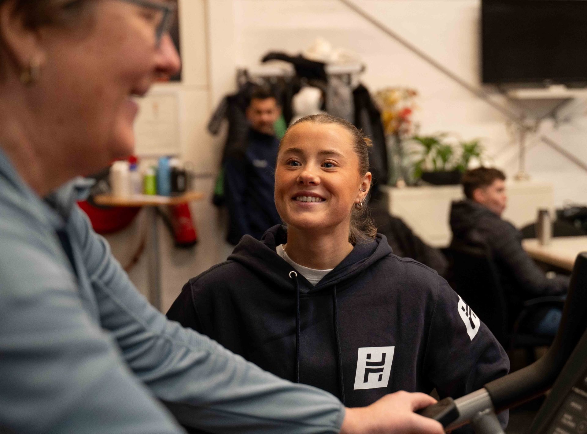 LeefstijlHUB coach glimlacht tijdens gesprek met deelnemer bij trainingstoestel